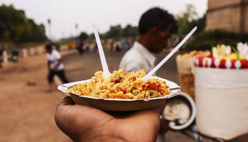 Ein Mann hält eine Einwegschale mit Straßenessen aus Delhi in der Hand