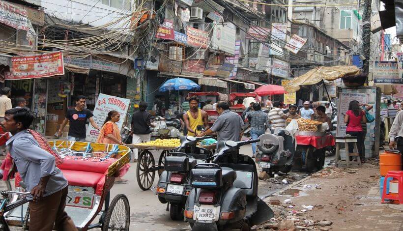 Das Bild zeigt eine chaotische Straße in Delhi mit Straßenverkäufern und vielen Menschen