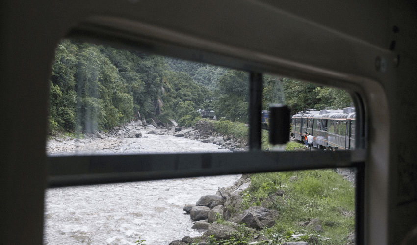 Ein Bild wo noch das Zugfenster rundum zu sehen ist und draußen einen Fluss zeigt und das hintere Ende des Zuges, weil er in eine Kurve einfährt.