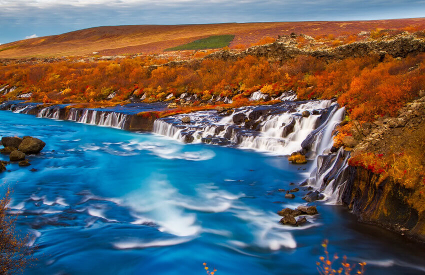 Ein Wasserfall mit vom Herbst gelb und braun gefärbten Pflanzen im Hintergrund.