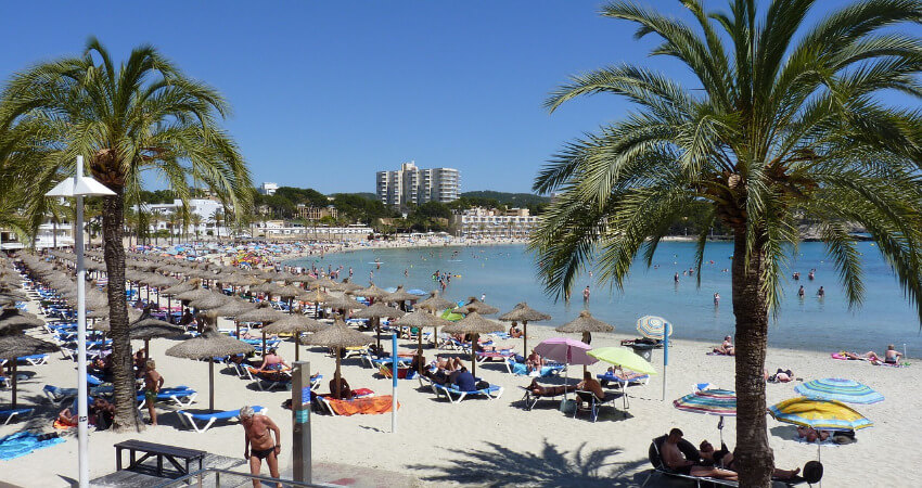 Ein langer Sandstrand mit vielen Stroh Sonnenschirmen.