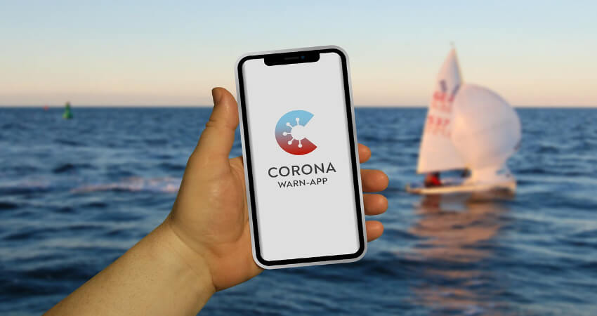 Ein Smartphone in der Hand mit der Corona-Warn-App und davor das Meer