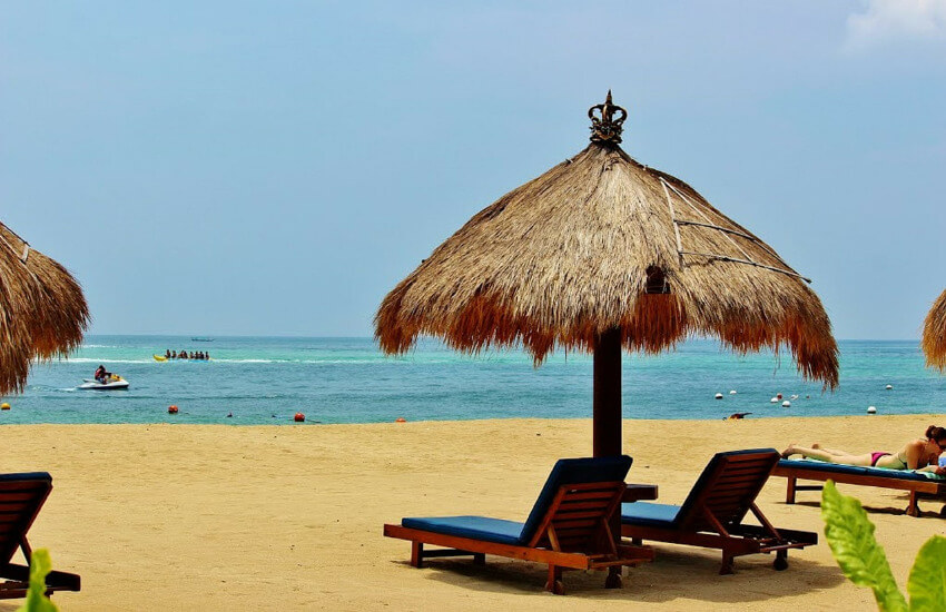 Zwei Liegen mit einem Sonnenschirm aus Stroh am Sandstrand von Bali.