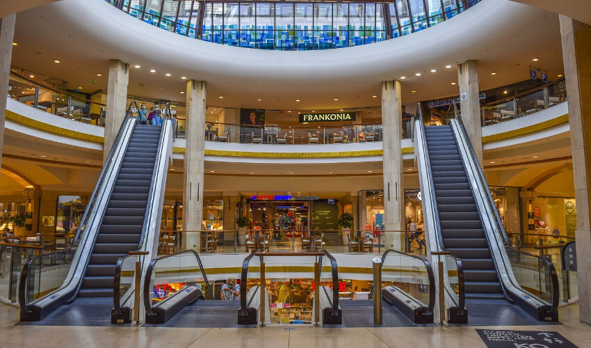 Rolltreppen in einem Einkaufszentrum. Links und rechts jeweils eine Rolltreppe, die nach oben führt und in der Mitte zwei, die nach unten laufen.