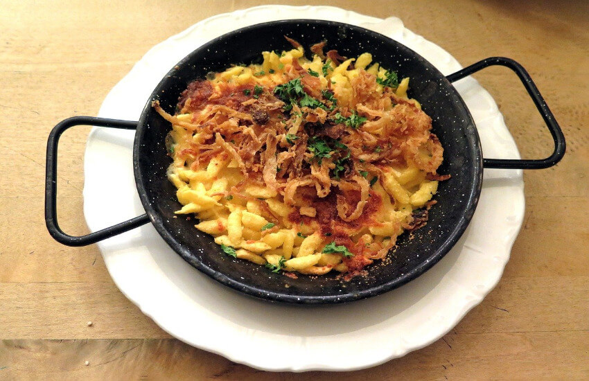 Käsespätzle mit gerösteten Zwiebeln in einer Pfanne serviert.