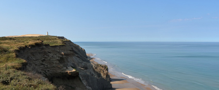 Eine hohe steile Felsklippe, darunter ein schmaler Sandstreifen.