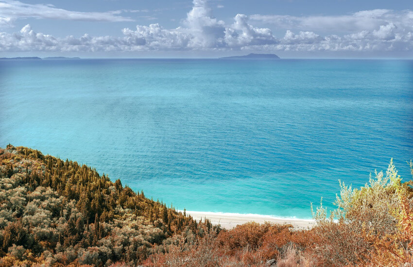 Ein toller Ausblick von einem mit Sträuchern bewachsenen Hügel auf den Strand und das türkise Meer.