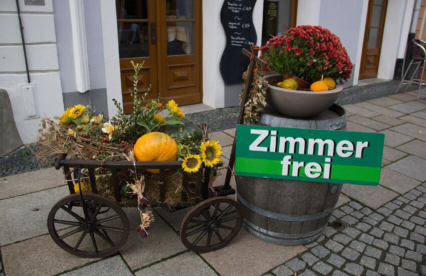 Ein Holzfass und ein Leiterwagen vor der Tür einer Pension mit einem Schild Zimmer frei.