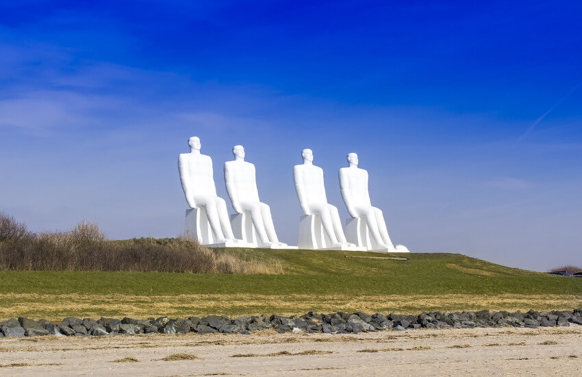 Vier große weiße Männerskulpturen am Strand von Esbjerg.