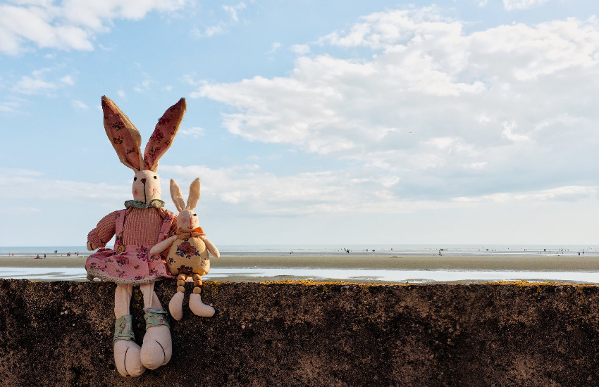 Ein gebastelter Osterhase in Menschengröße und einer in Kindergröße sitzen auf einer Betonmauer an der Ostsee.