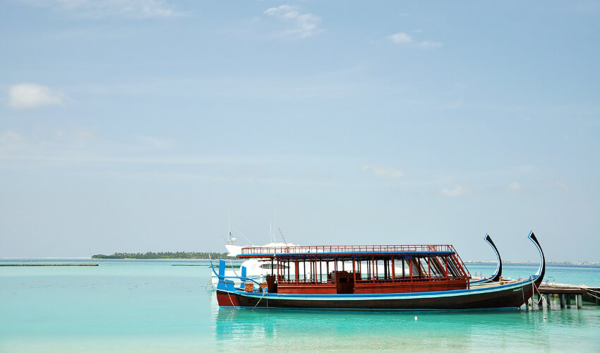 Ein Dhoni-Boot mit schwarzem Rumpf und Holzaufbau ankert an einem Steg auf den Malediven.