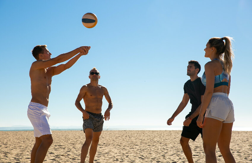 Drei Männer und eine Frau spielen am Stand Volleyball ohne Netz.
