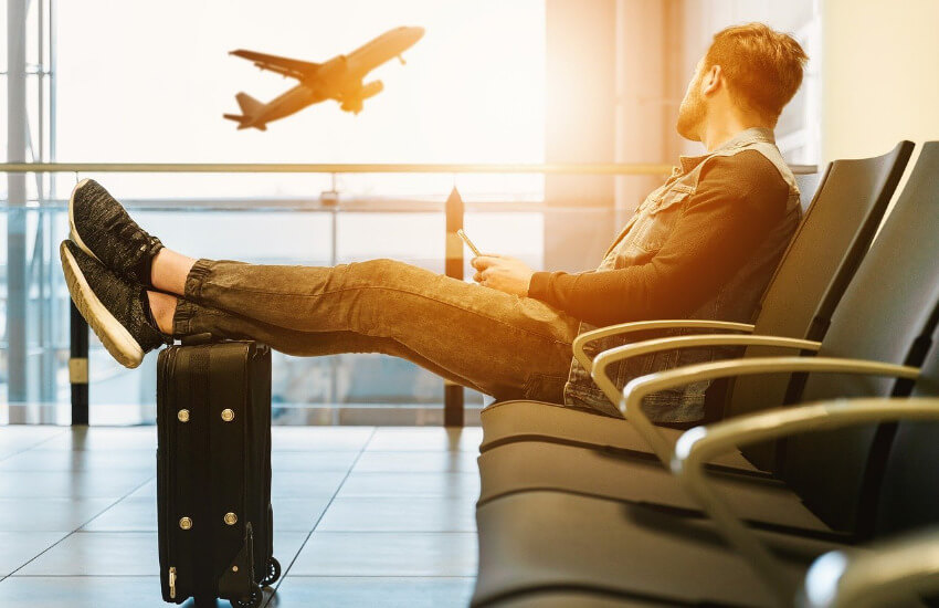 Ein Passagier wartet am Flughafen auf seinen Abflug und schaut Richtung Fenster, wo gerade ein Flugzeug abhebt.