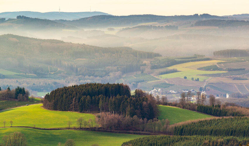 Eine hügelige Landschaft mit abwechselnd Wiesen, Felder und Wald.