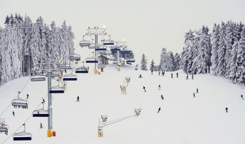 Ein Sessellift im Winterbetrieb mit einer Skipiste rechts daneben.