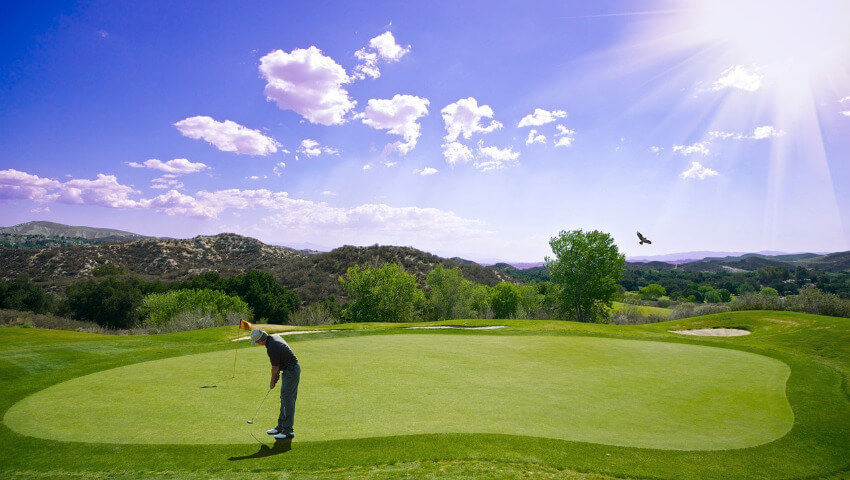 Ein Golfspieler schlägt den Ball unter Sonnenschein Richtung der Fahne.