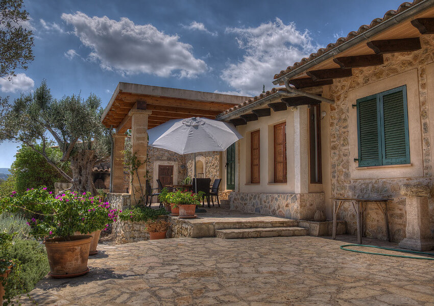 Eine Finca aus Stein mit einer kleinen Terrasse vor einem Blumengarten.