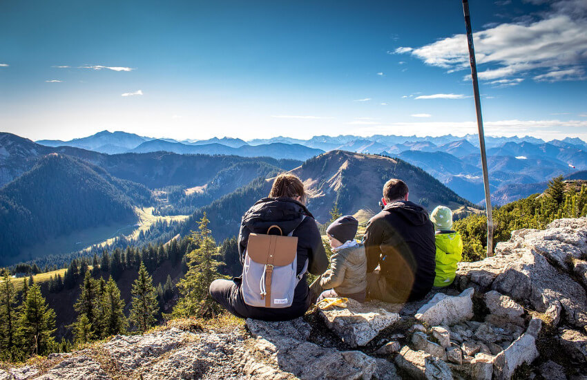 Eltern sitzen mit zwei Kindern am Berg auf Steinblöcken und genießen die Aussicht der österreichischen Berge.