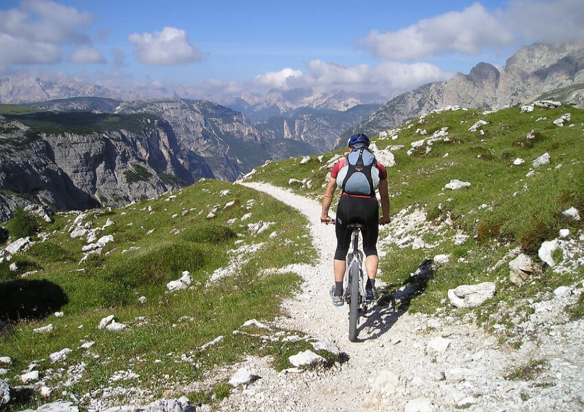 Ein Mountainbiker unterwegs auf einem kleinen steinigen Weg in den Alpen.