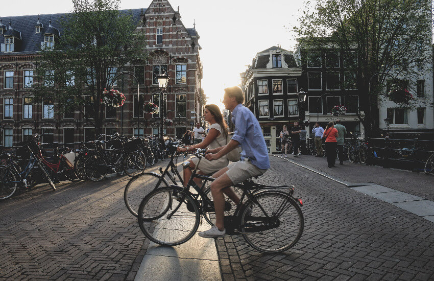 Ein Mann und eine Frau fahren nebeneinander in der Altstadt von Amsterdam mit dem Fahrrad.