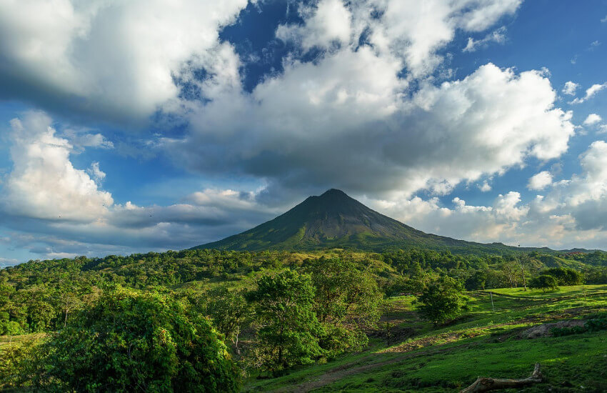 Der von Wolken und Nebel umgebene Vulkan Arenal in Costa Rica, umgeben von dichtem, grünem Regenwald unter einem bewölkten Himmel.