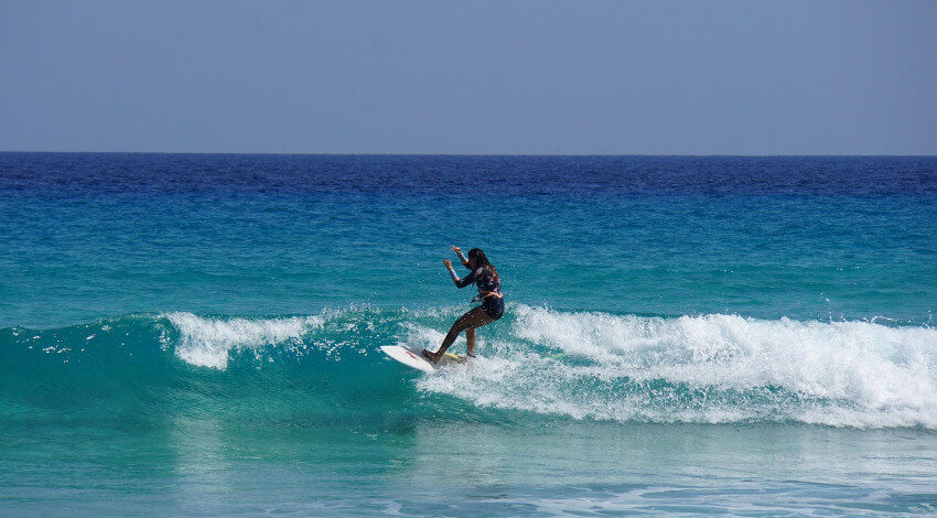 Fuerteventura Surfen Frau mit Surfbrett beim Surfen auf einer Welle im türkisblauen Meer vor Fuerteventura.